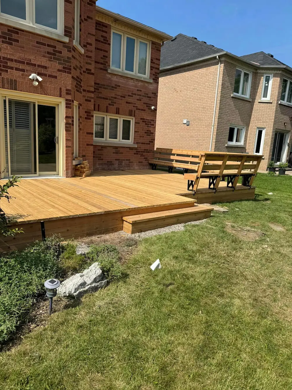 Large, low-profile backyard timber deck featuring custom built-in bench seating with industrial black metal brackets.