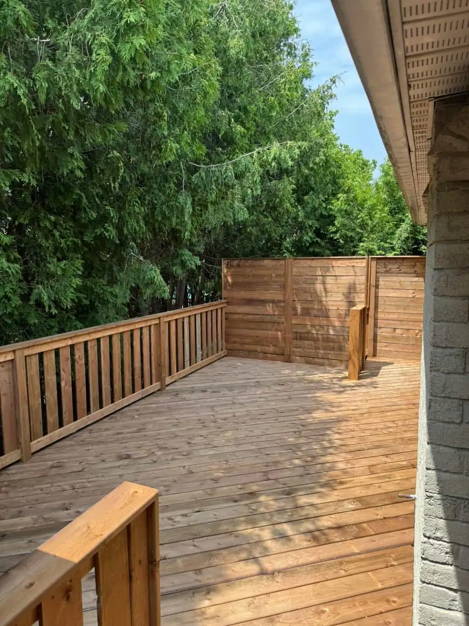 Spacious wooden deck featuring a custom horizontal plank privacy screen and vertical wood railing overlooking a lush backyard