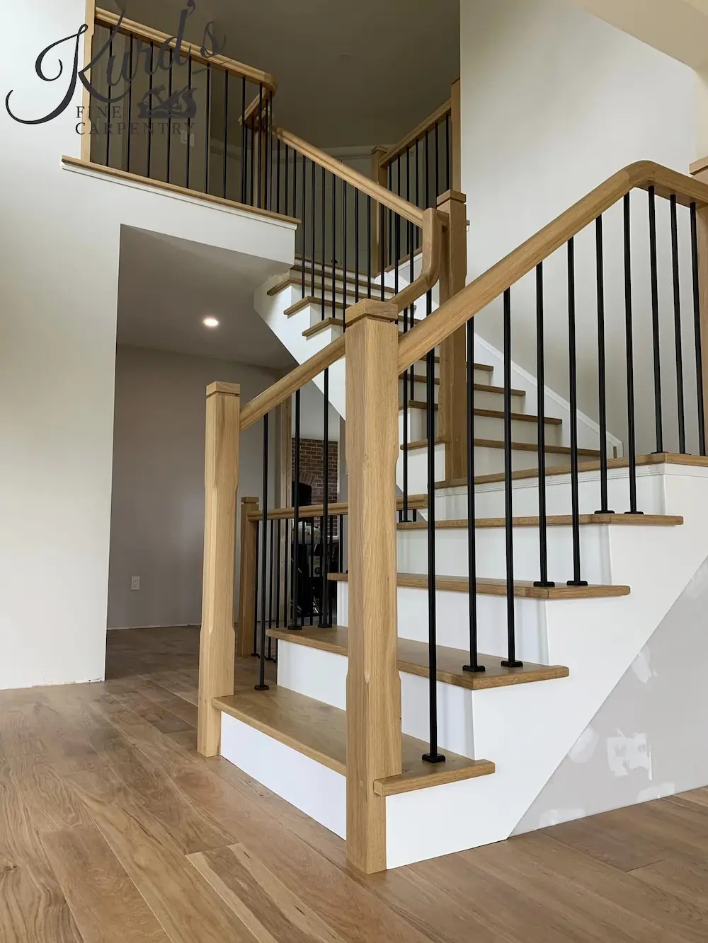Close-up of a renovated staircase featuring white oak newel posts and handrails, white risers, and sleek black metal spindles.